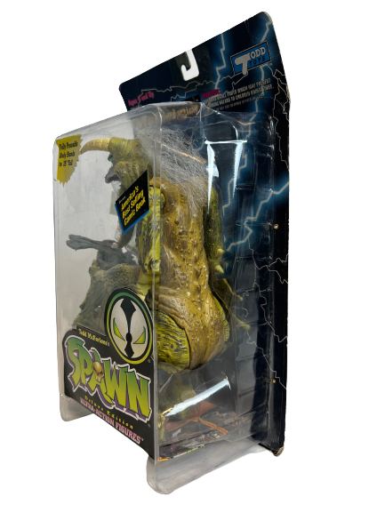 The side of a clear box containing a green dinosaur action figure with scaly skin. The text on the box says SPAWN and has blue lightning in the background..