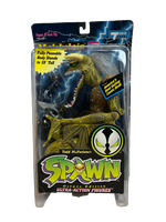A plastic box with blue lightning containing a green dinosaur actoin figure with a wide open mouth showing a set of sharp teeth, green wings, and scaly skin. The text on the box says fully posable body Stands to 18" tall. SPAWN Ultra-Action Figures.