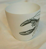 A side view of a white porcelain votive candle vase featuring a black and white lobster design from the brand Two's Company. The lobster's claws and head are visible.